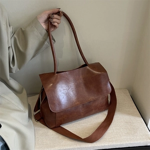 Brown vintage leather tote bag with wide shoulder strap and textured finish on a stone surface