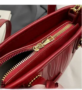 Detailed close-up of smooth gold metal zipper on red textured leather bucket wedding bag