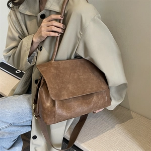 Brown vintage faux leather tote bag with wide strap worn by model in trench coat