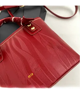 Close-up of red textured leather bucket bag with elegant wave embossing and golden hardware