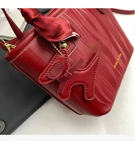 Close-up of red textured leather bridal bucket bag with bow and golden deer charm