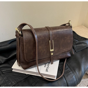 Détail d'un sac bandoulière rétro en cuir marron avec boucle dorée et fini texturé