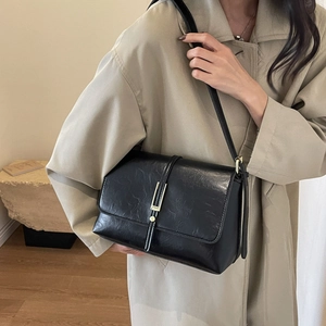 Sac bandoulière vintage noir en similicuir avec boucle dorée porté par un mannequin en manteau