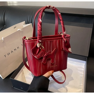 Detailed gift box presentation of a red bridal bucket bag with silk scarf handle and puppy charm