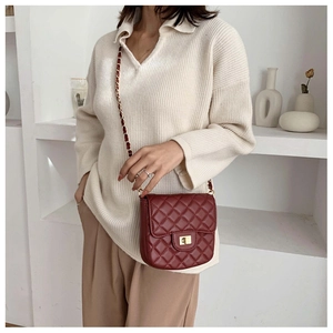 Detail of burgundy quilted crossbody bag with golden chain strap on a model
