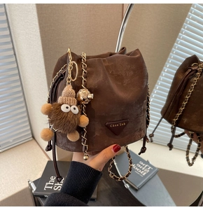 Detail of a dark brown suede bucket bag with chain strap and luxury lucky bag drawstring