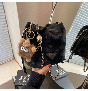 Detail of black drawstring bucket bag with gold chain strap and plush monster charm