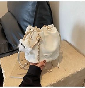 Detail of white drawstring bucket bag with chain strap and plush monster charm