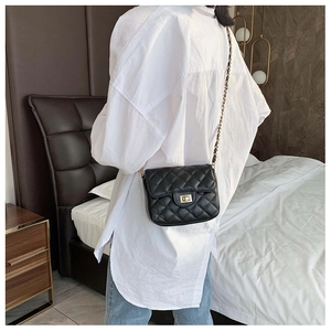 Detail of black quilted crossbody bag with golden metal lock and chain strap on model