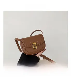 Close-up of brown litchi grain leather saddle bag featuring a vintage gold metal clasp