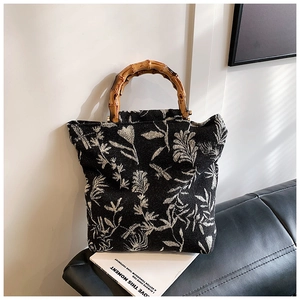 Close-up of bamboo handles on a black canvas tote with white floral embroidery