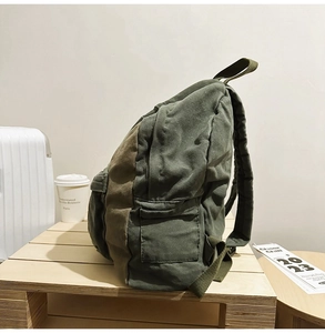 Detailed side view of olive green canvas backpack with functional flap side pockets