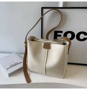 Detail view of cream bucket bag showing fine faux leather texture and brown strap
