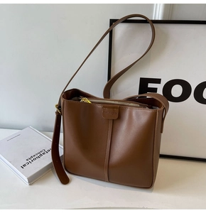 Detail of a brown leather bucket bag with vertical stitching and embossed strap accents