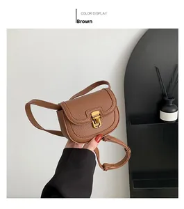 Detail view of a brown pebbled leather mini saddle bag with a golden snap closure