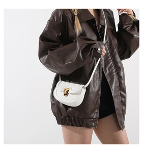 White mini saddle bag in lychee leather worn with a brown jacket for spring style
