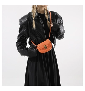 Detail of a bright orange mini saddle bag with vintage metal buckle and pebble leather texture