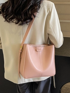 Minimalist pink leather bucket bag with adjustable strap shown on model in white suit