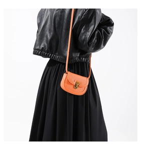 Detail of bright orange lychee grain leather saddle bag with vintage gold metal buckle