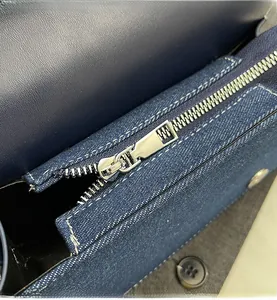 Close-up of smooth silver metal zipper on dark blue denim handbag with fine stitching
