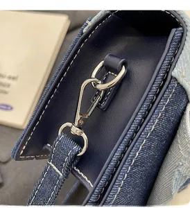 Close-up of silver metal hardware hook and blue denim stitching on the crossbody bag