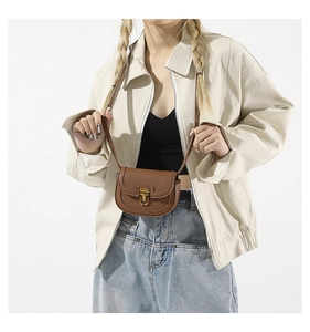 Detailed close-up of a brown pebble leather saddle bag with vintage gold metal clasp