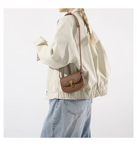 Close-up of brown litchi pattern saddle bag with vintage gold metal buckle on model