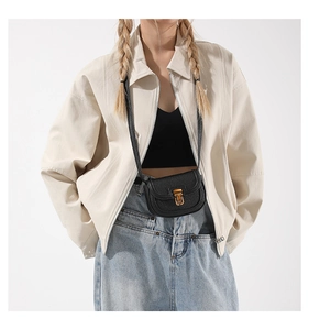 Detail of black pebbled leather mini saddle bag with golden lock on a white jacket