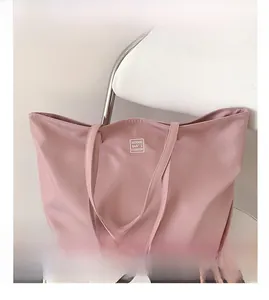 Detail shot of pink nylon tote bag showing brand logo patch on a white chair