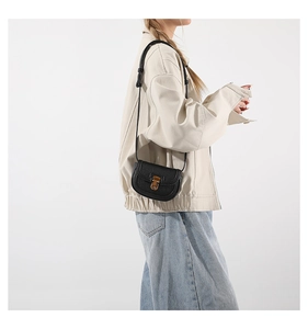 Detail view of a black mini saddle bag with golden buckle and grainy leather texture