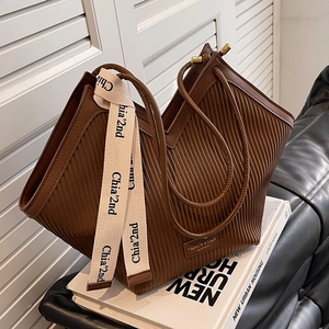Brown pleated PU leather tote bag with brand ribbon on architectural books