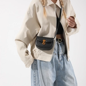 Retro black leather saddle cross-body bag with gold buckle shown on model in studio