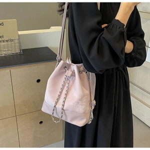 Detail of pink faux suede bucket bag with chain drawstring and matching strap on model
