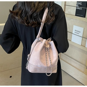 Modern light pink drawstring bucket bag with silver chain worn as a stylish crossbody bag