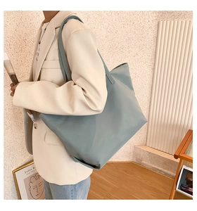Large misty blue nylon tote bag worn by a model in a minimalist indoor setting