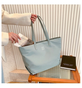 Detail showing high capacity of a light blue nylon tote bag with square logo and magazine