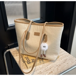 Detail of cream tote bag featuring embossed cartoon patterns and brown leather handle