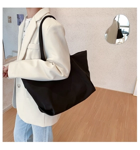 Detail view of a large black nylon tote bag worn by a model in a minimalist setting