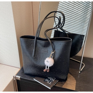 Detail of black faux leather tote bag featuring love letter embossing and a white pompom charm