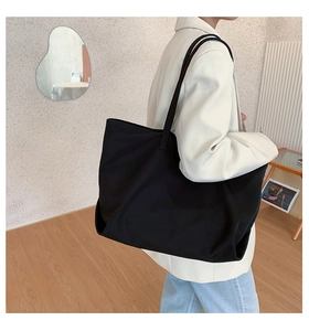 Minimalist black nylon tote bag worn by a model in a modern indoor studio setting