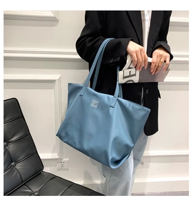 Detail of light blue nylon tote bag worn by a model in a professional casual outfit