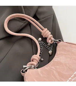 Detailed close-up of pink shoulder bag with metallic charms and knotted strap detail