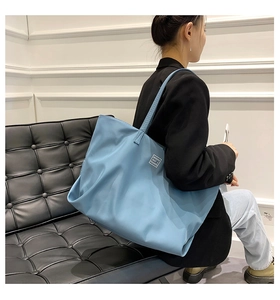 Minimalist blue nylon tote bag with fashion patch on shoulder of seated model