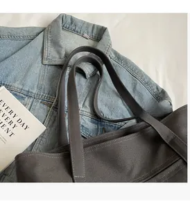 Detail of grey canvas tote bag with reinforced handles on denim jacket background