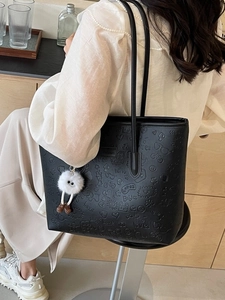 Classic black embossed tote bag with unique pattern and white plush charm on a model