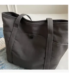Close-up of a dark grey canvas tote bag showing outer pocket texture and snap button closure