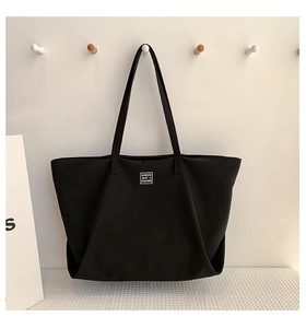 Close-up of a black tote bag with white logo label hanging on a minimalist white wall