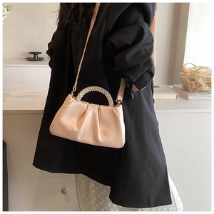 Detail of a creamy white pleated cloud bag with pearl handle and leather shoulder strap