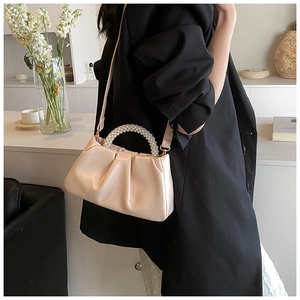 Detail of a creamy beige cloud clutch bag with pearl handle and leather shoulder strap