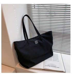 Detail of a black nylon tote bag with logo patch against white shutters and art book